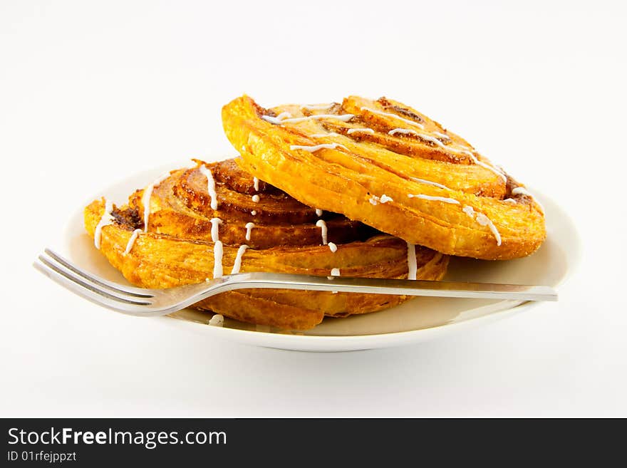 Two cinnamon buns on a plate with a fork with a clipping path on a white background. Two cinnamon buns on a plate with a fork with a clipping path on a white background