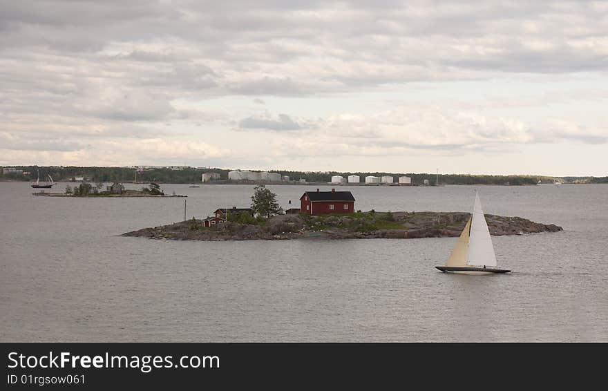 A view from the island of Luoto just across the bay from Helsinki, Finland. View is of a sailboat touring the area with a typical fisherman's cottage in the Baltic Sea in the Bay of Finland. A view from the island of Luoto just across the bay from Helsinki, Finland. View is of a sailboat touring the area with a typical fisherman's cottage in the Baltic Sea in the Bay of Finland.