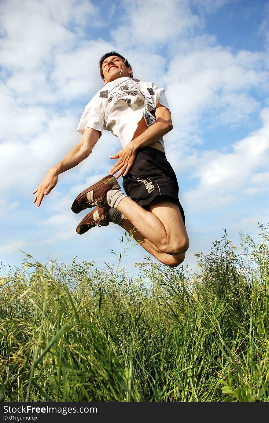 Man jumping on a green meadow with a beautiful cloudy sky. Man jumping on a green meadow with a beautiful cloudy sky