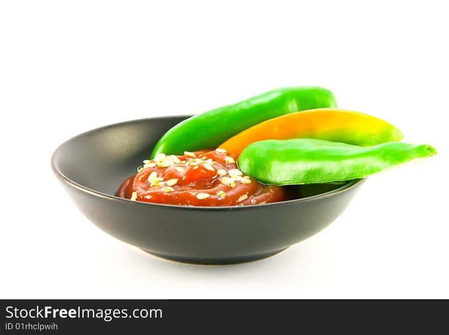 Whole chillis in a black bowl with red chilli dipping sauce with clipping path on a white background. Whole chillis in a black bowl with red chilli dipping sauce with clipping path on a white background