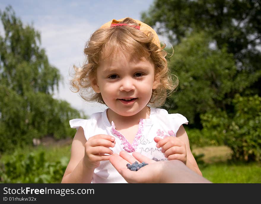 Beautiful little girl eating honeysuckle in the garden