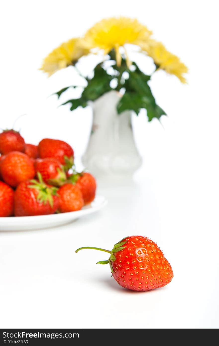 Fresh strawberry against a plate with berries and vases with the flowers. Fresh strawberry against a plate with berries and vases with the flowers