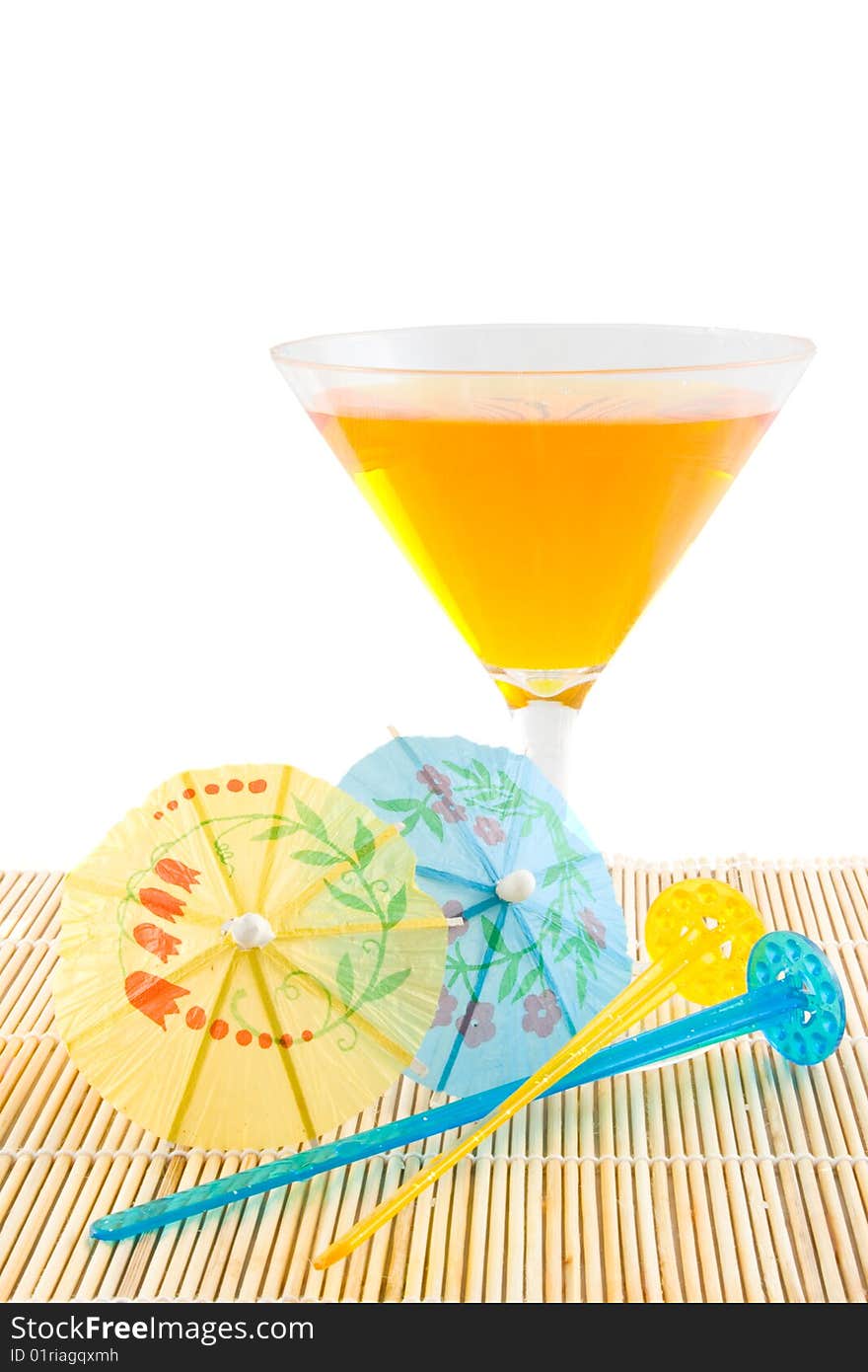 Orange cocktail on bamboo placemat with stearing sticks and small parasols on white