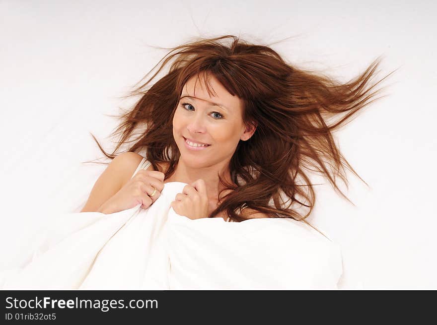 Woman lying in bed smiling with a lot of copy-space on the white blanket. Woman lying in bed smiling with a lot of copy-space on the white blanket