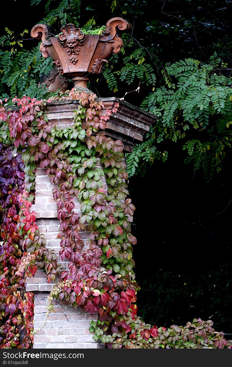 A brick pillar with vegetable mantle, holding an ancient earthenware vase. Ancient castle in Italy, Oltrepo Pavese, Montalto. A brick pillar with vegetable mantle, holding an ancient earthenware vase. Ancient castle in Italy, Oltrepo Pavese, Montalto.