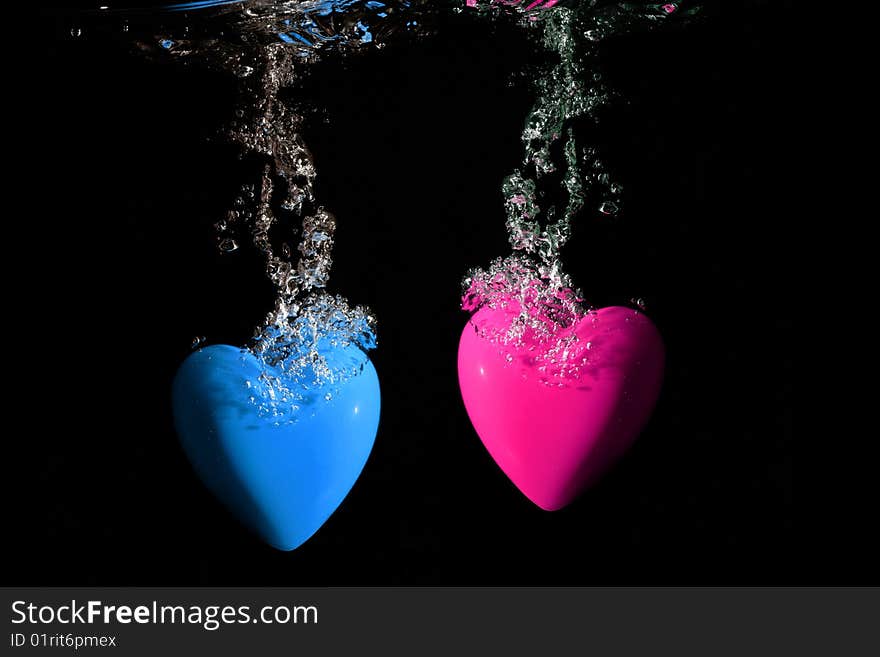 Pink and blue hearts splashing underwater against black background. Pink and blue hearts splashing underwater against black background