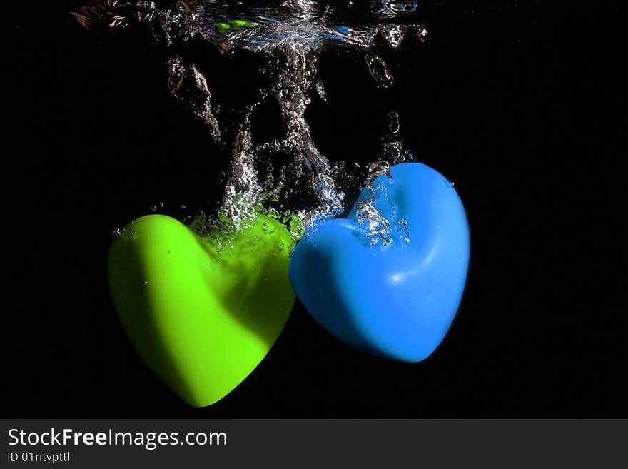 Green and blue Hearts splashing underwater against black background. Green and blue Hearts splashing underwater against black background