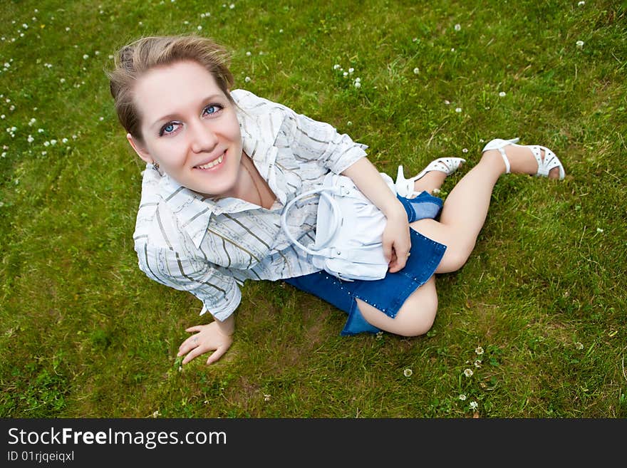 Beautiful young woman sits on a green grass