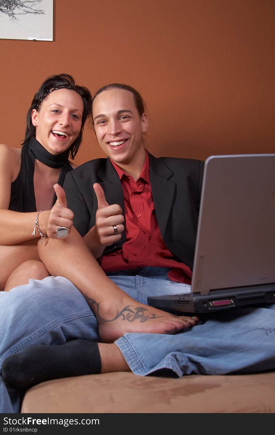 Young couple on the couch surfing the web with their laptop - showing a thumbs up sign. Young couple on the couch surfing the web with their laptop - showing a thumbs up sign.