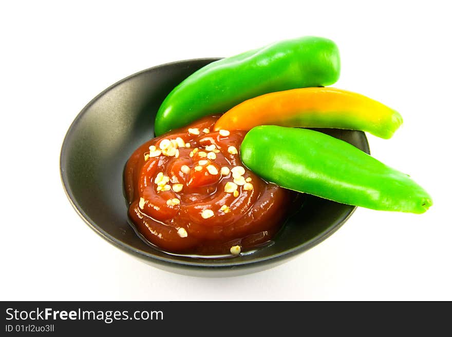 Whole chillis in a black bowl with red chilli dipping sauce with clipping path on a white background. Whole chillis in a black bowl with red chilli dipping sauce with clipping path on a white background