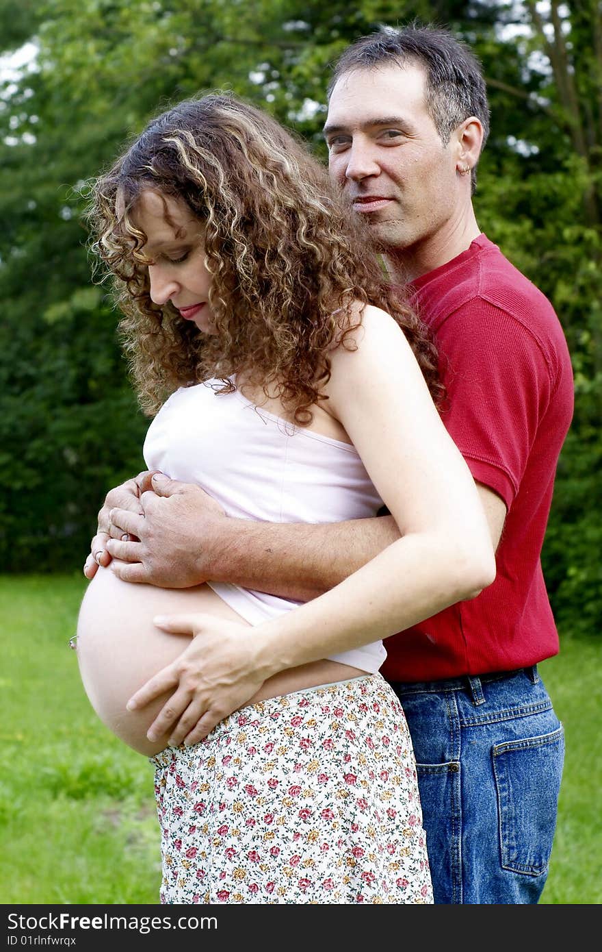 A happy, young pregnant couple sharing an embrace with exposed belly.