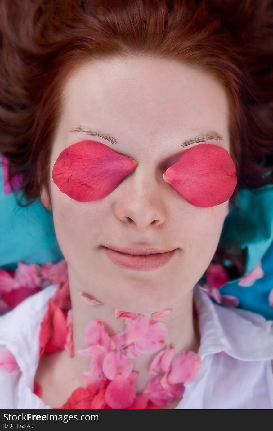 Portrait of young woman with pink petals in front of eyes. She is looking through flowers and smiling. Some petals laying on her neck. White blouse. Shallow depth of field. Portrait of young woman with pink petals in front of eyes. She is looking through flowers and smiling. Some petals laying on her neck. White blouse. Shallow depth of field.