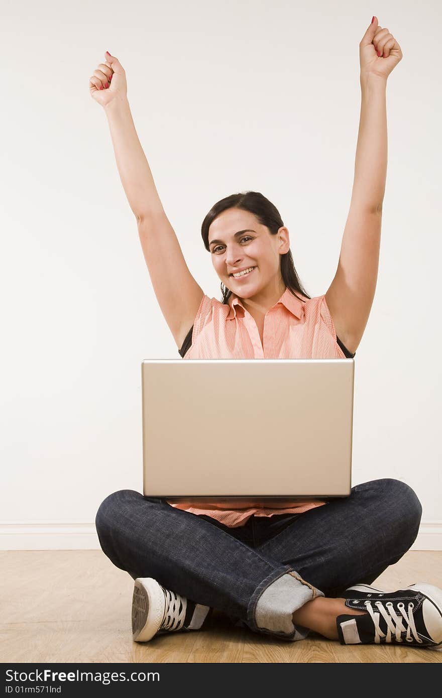 Young woman seated on floor with laptop and arms raised with excitement. Young woman seated on floor with laptop and arms raised with excitement