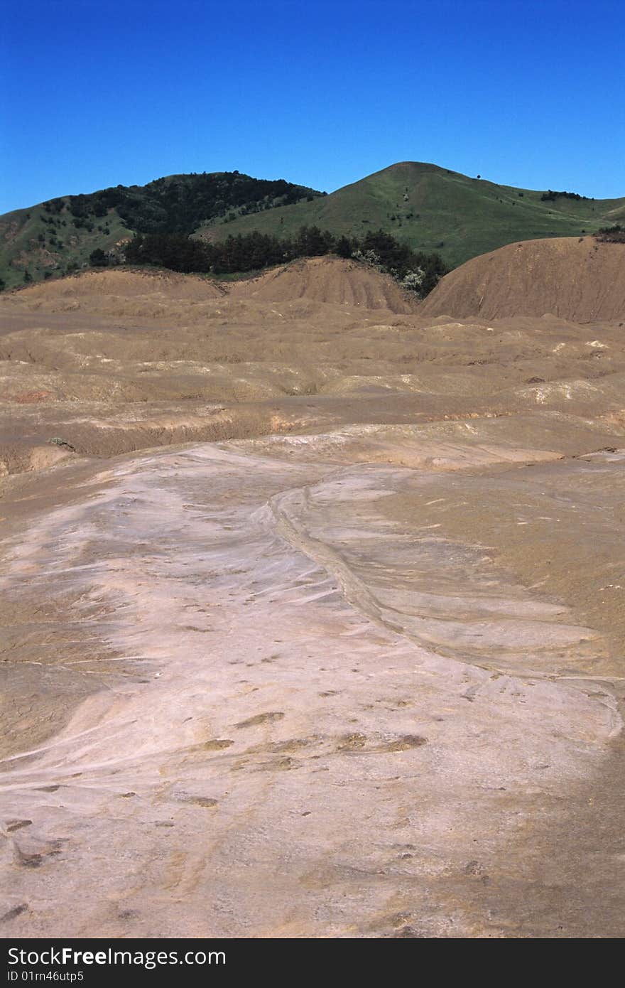 Brown volcano with green hills and blue sky in background