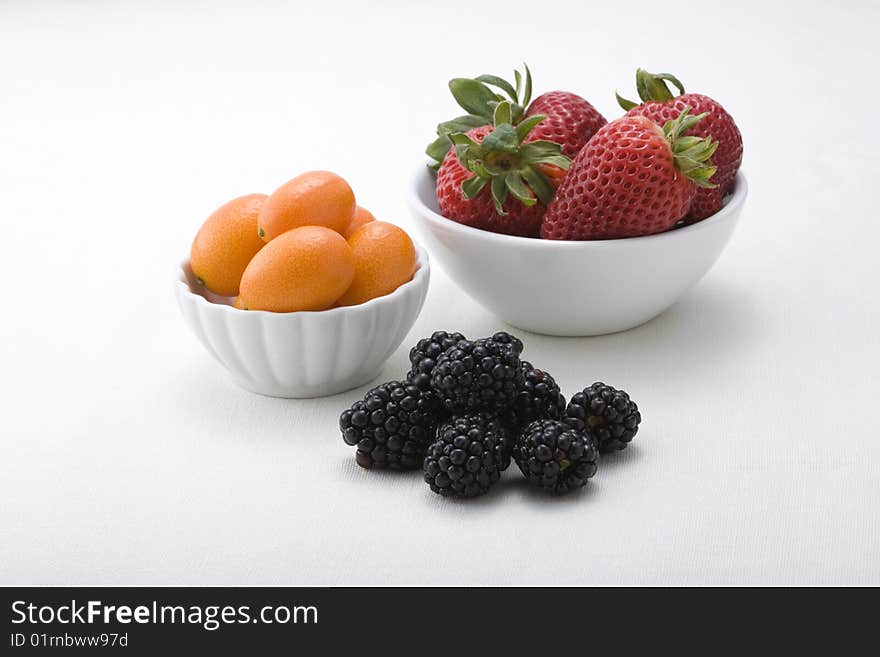 Bowls of delicious strawberries, kumquats, and blackberries at the peak of freshness. Bowls of delicious strawberries, kumquats, and blackberries at the peak of freshness