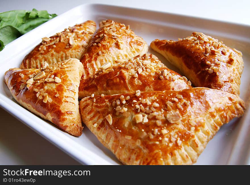 A white dish with baked puff-pastry pasties filled in fresh sorrel with sugar and peanut, blur background