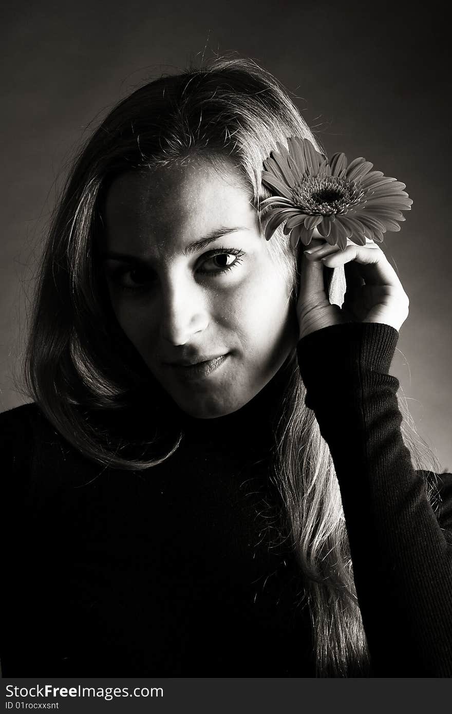 A young beautiful girl in dark  jumper posing with a flower in her hand. A young beautiful girl in dark  jumper posing with a flower in her hand