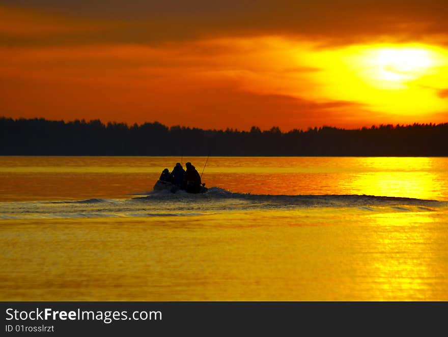 Sunset and motor boat with three persons going to fish