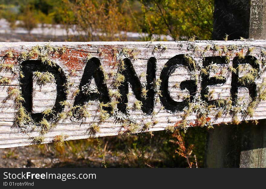 Old wooden danger sign covered by moss