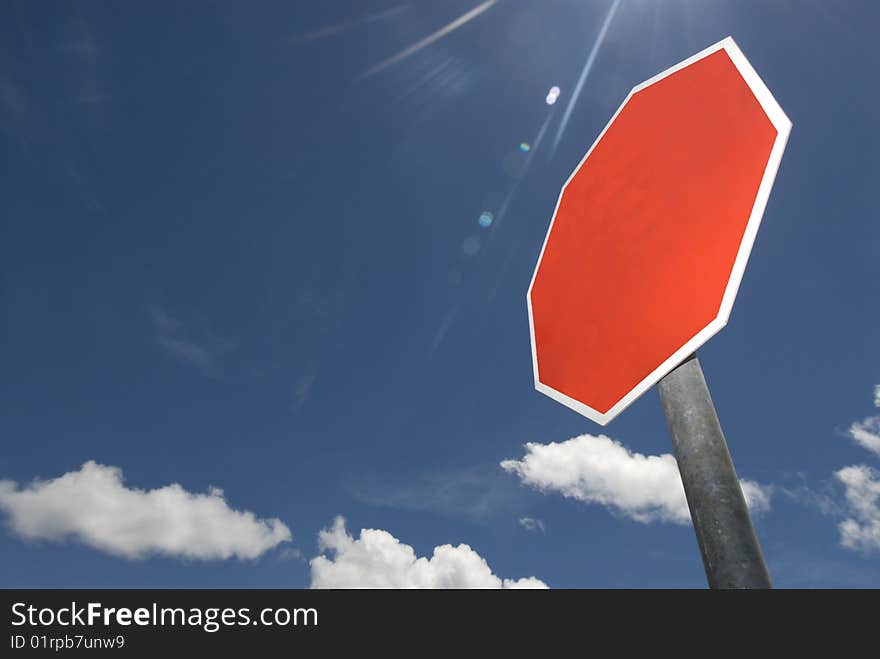 Bright red blank sign with space for lettering set against blue sky with sunlight filtering down