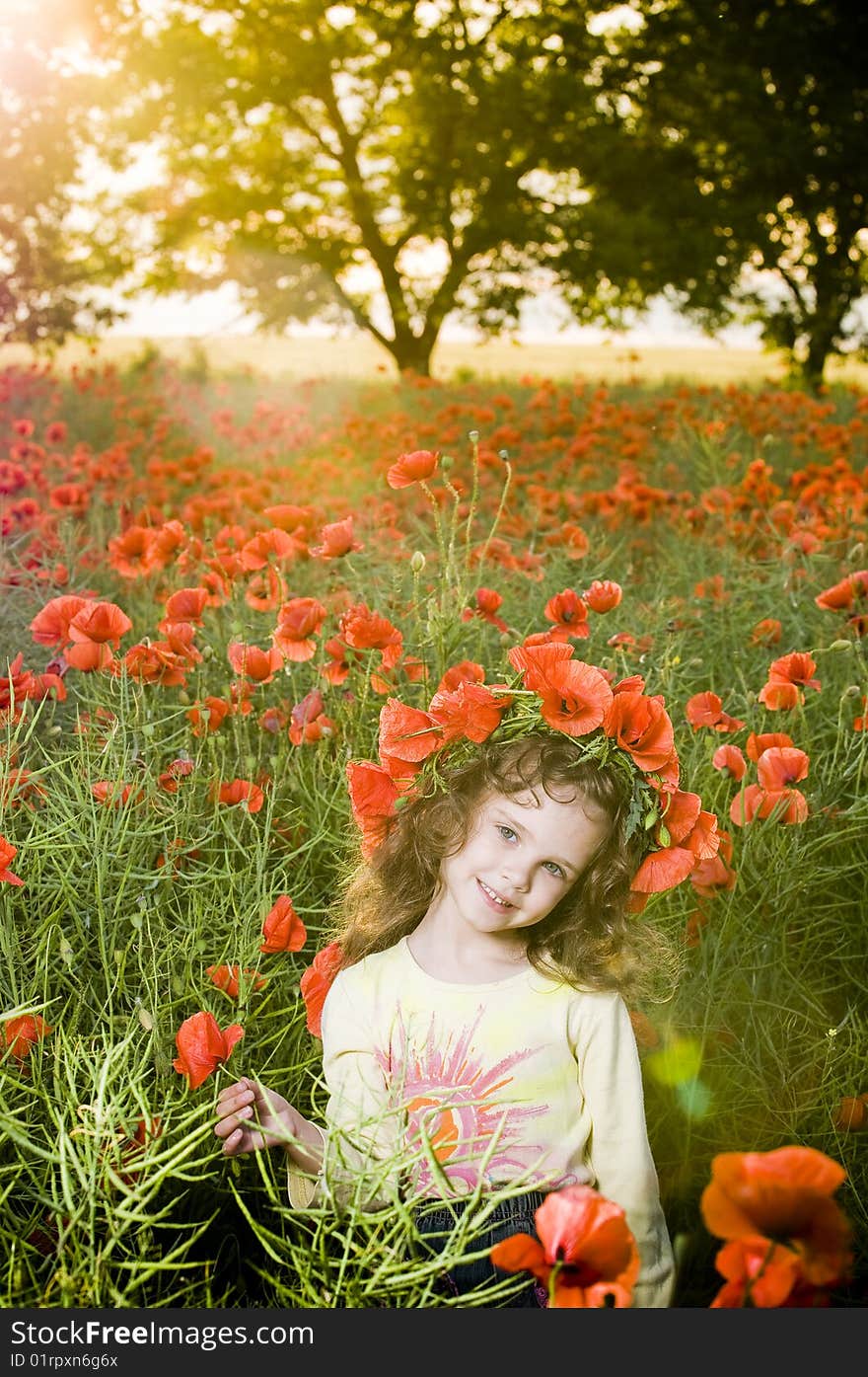 Smiling little girl with flower garland in the poppy field at sunset. Smiling little girl with flower garland in the poppy field at sunset