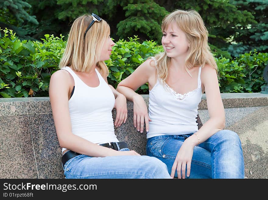 Two girls talk sitting on a bench in park. Two girls talk sitting on a bench in park