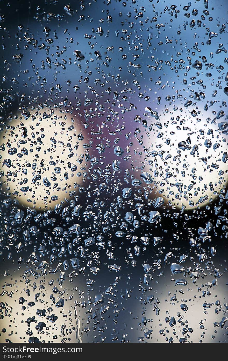 An out of focus lights of a car and a glass with many rain drops. An out of focus lights of a car and a glass with many rain drops.