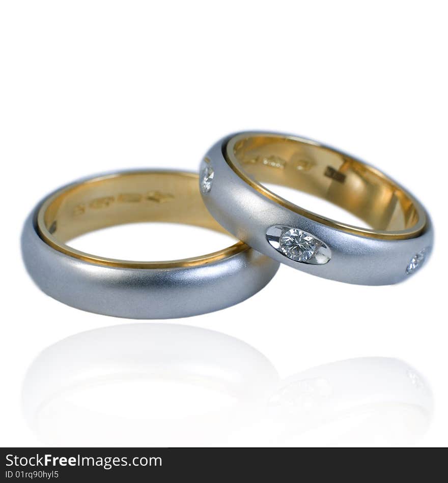 His and hers golden wedding bands, with diamonds. On a white background with soft reflection, isolated. His and hers golden wedding bands, with diamonds. On a white background with soft reflection, isolated.