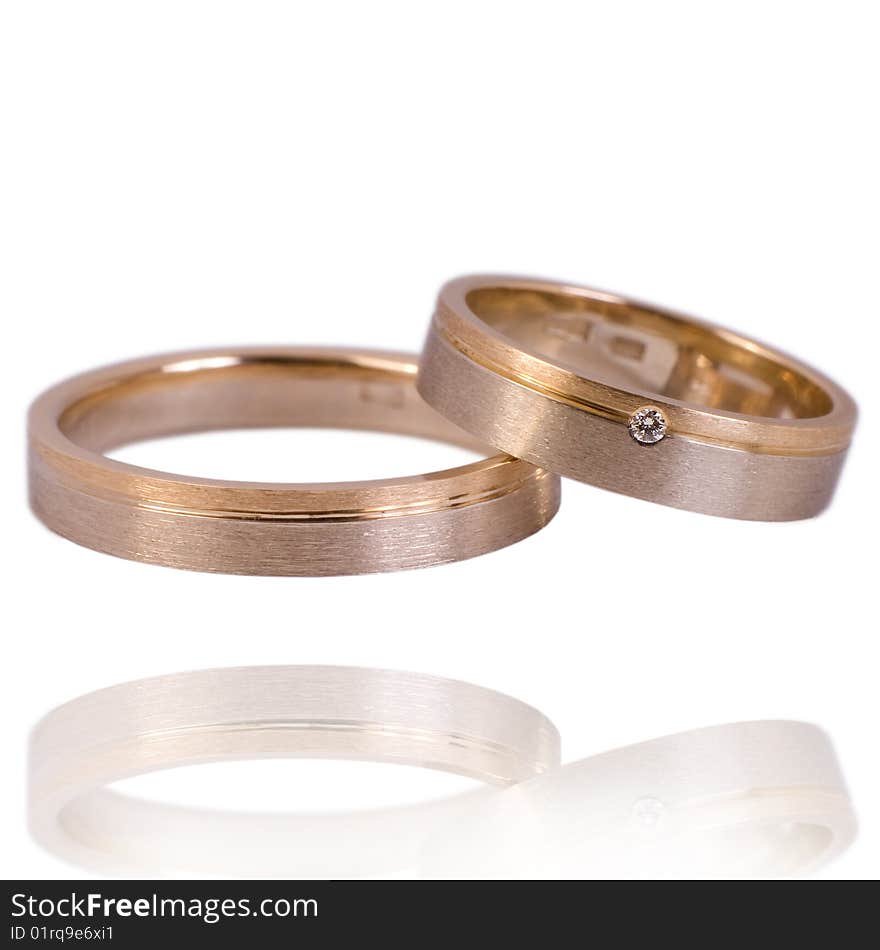 His and hers golden wedding bands, with diamonds. On a white background with soft reflection, isolated. His and hers golden wedding bands, with diamonds. On a white background with soft reflection, isolated.