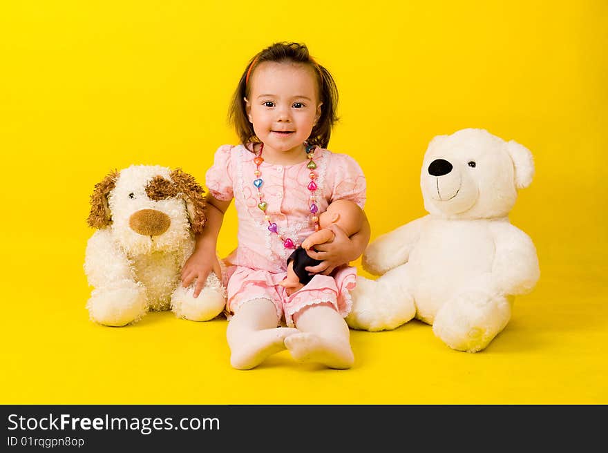 Cute little girl with toys on the floor over yellow.