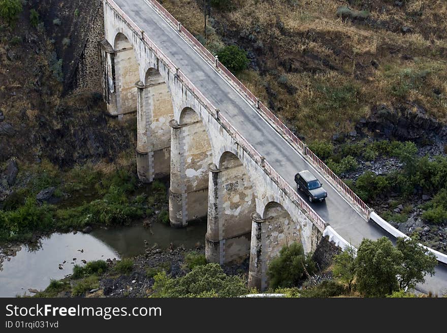 Top view of a arc stoned bridge over a river with a car passing by. Top view of a arc stoned bridge over a river with a car passing by.