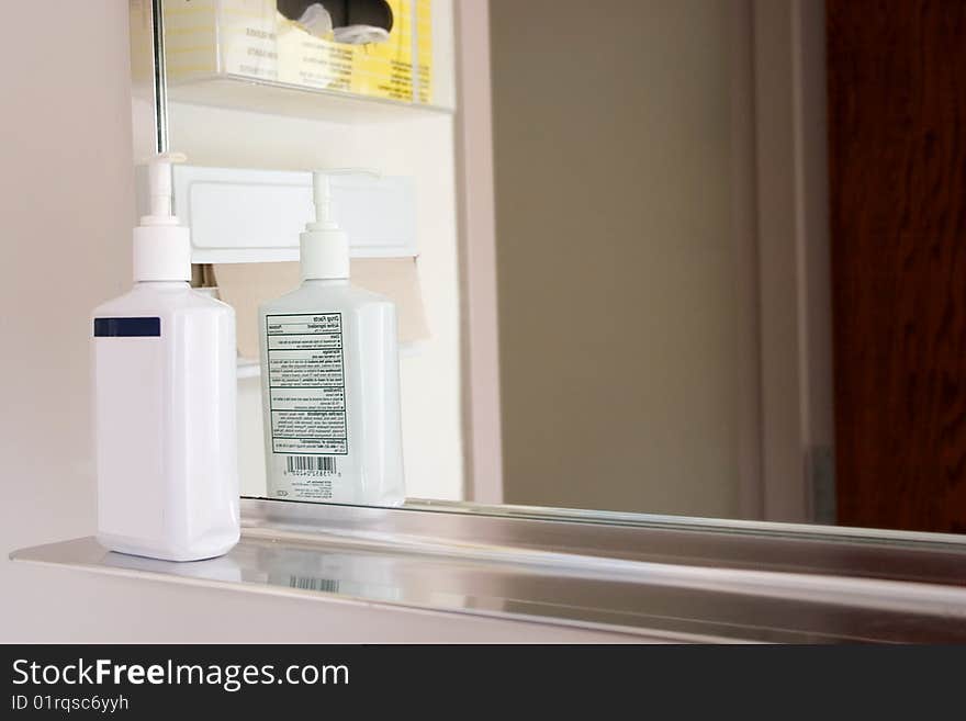 A bottle of hand soap setting on a shelf by a mirror