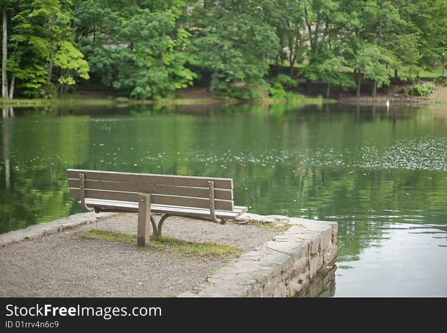 Empty wooden park bench sitting by the lake in the summer time. Empty wooden park bench sitting by the lake in the summer time