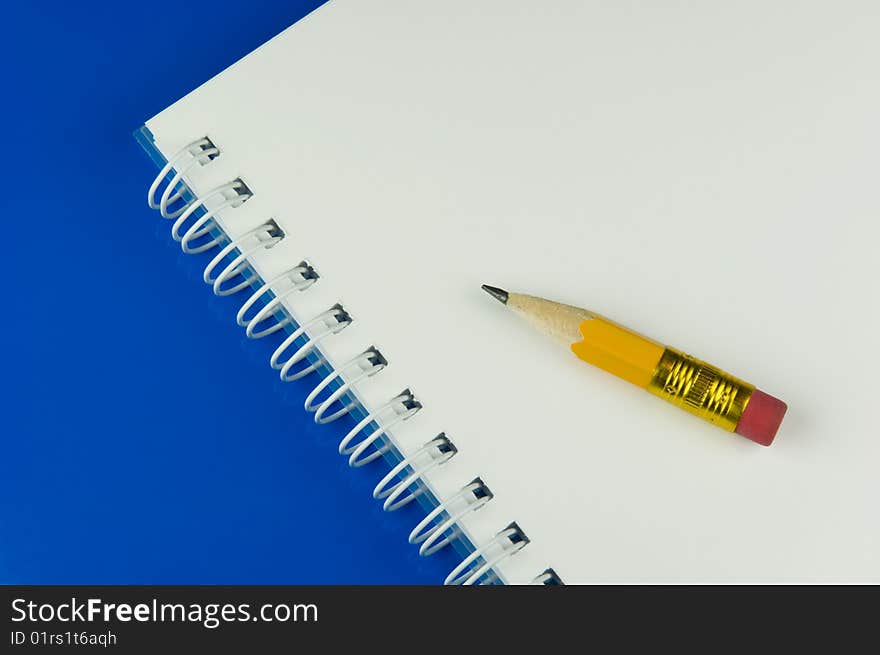 Short yellow pencil on a notepad, blue table