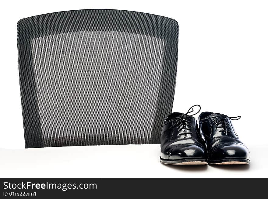 A pair of black formal business dress shoes on a white desk by a chair. A pair of black formal business dress shoes on a white desk by a chair