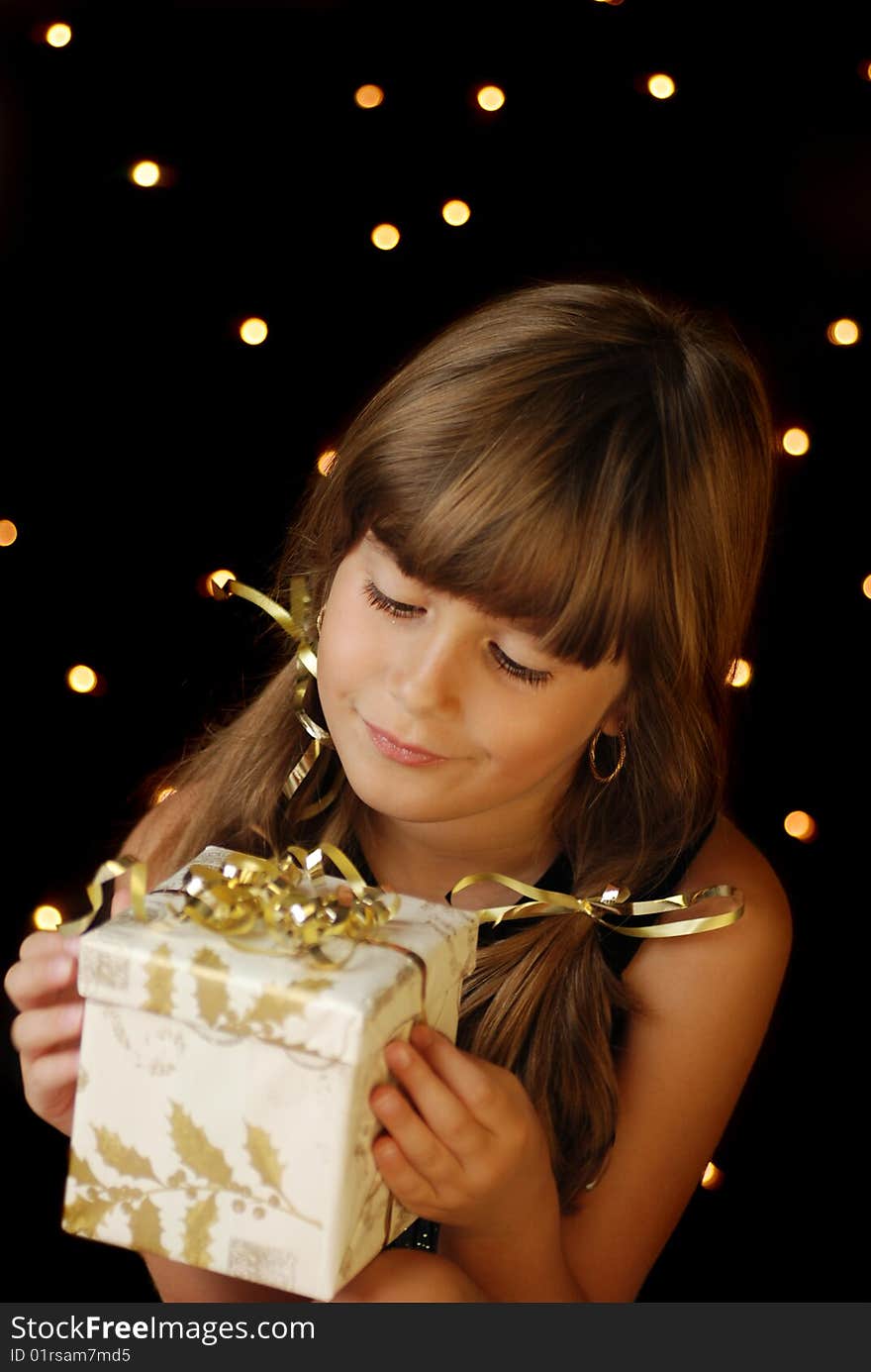 A cute young girl holding a christmas gift, dark background with christmas light bokeh