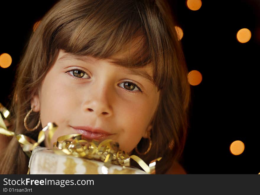 A beautiful young girl holding a gift, dark background with christmas light bokeh. A beautiful young girl holding a gift, dark background with christmas light bokeh