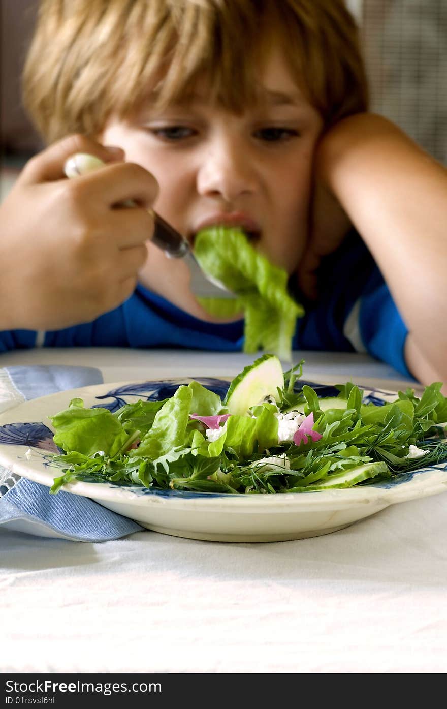 Young boy sits in front of a salad. Young boy sits in front of a salad