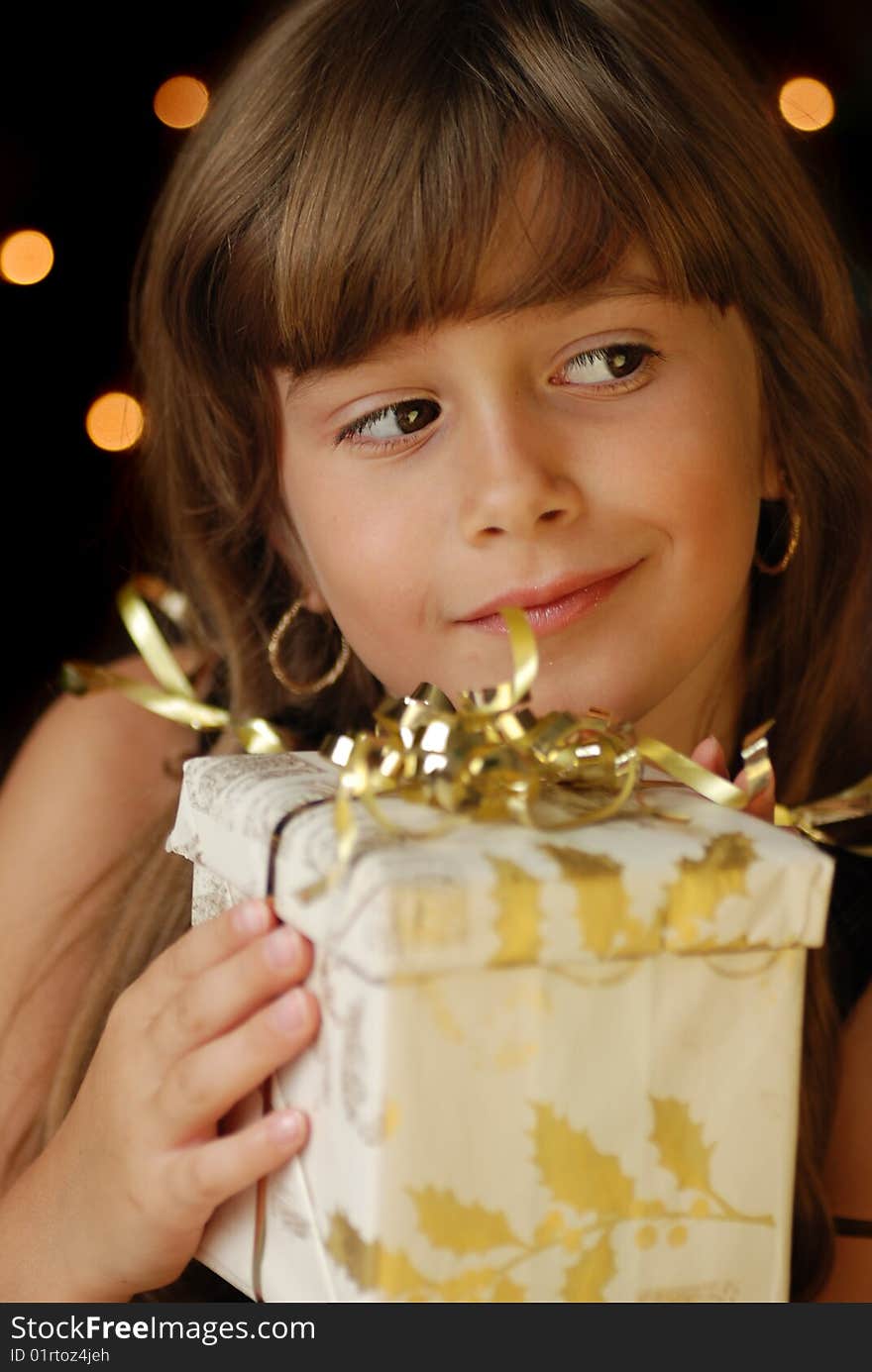 A cute young girl holding a christmas gift, dark background with christmas light bokeh. A cute young girl holding a christmas gift, dark background with christmas light bokeh