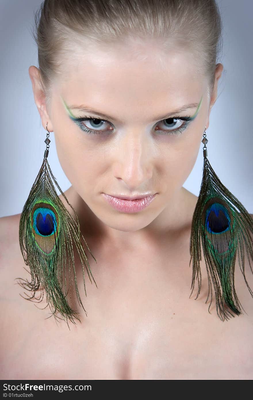 Close-up young blonde model with peacock earrings posing with beautiful make-up. Close-up young blonde model with peacock earrings posing with beautiful make-up