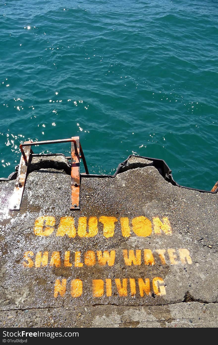 Above view image of a stenciled shallow water warning sign at the end of a breakwater. Above view image of a stenciled shallow water warning sign at the end of a breakwater.