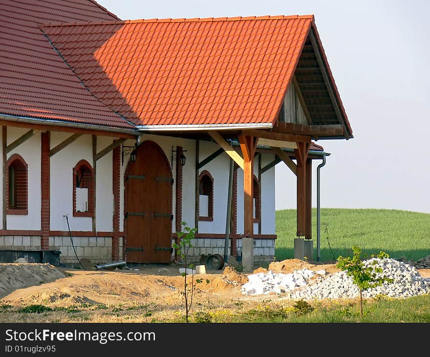 A view of new white farmhouse with big gate and red roof. Pieces of bricks in the front of the farmhouse.