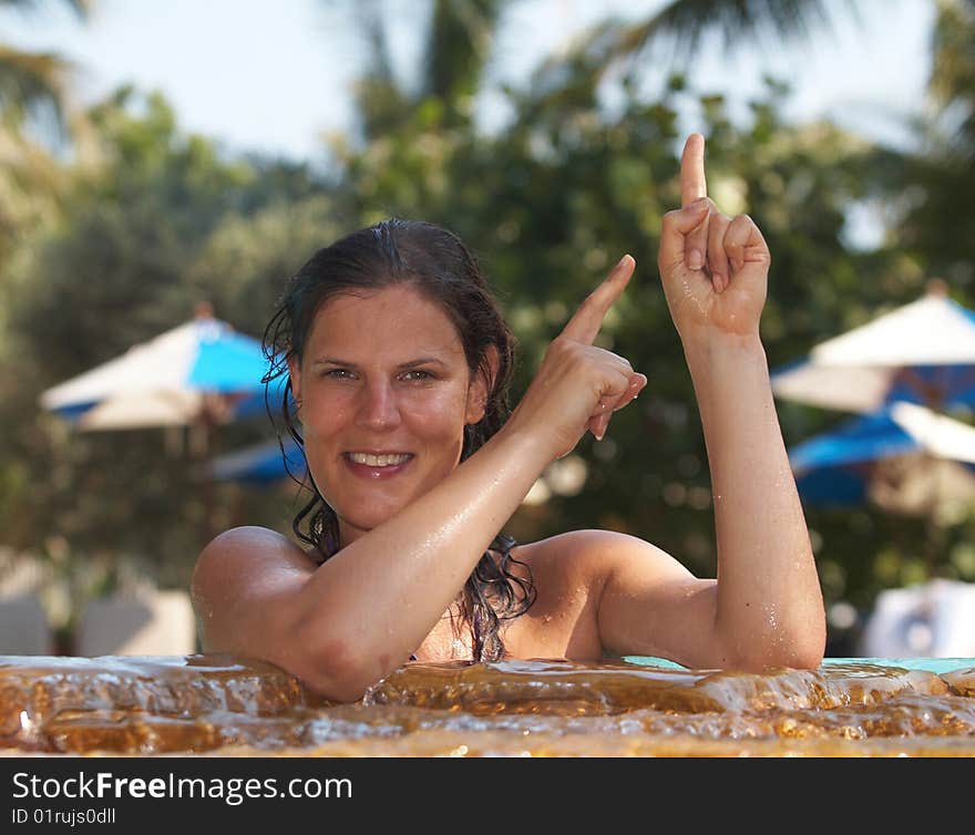 Young woman in a beautiful pool with palms in the background. She is pointing up. Young woman in a beautiful pool with palms in the background. She is pointing up.