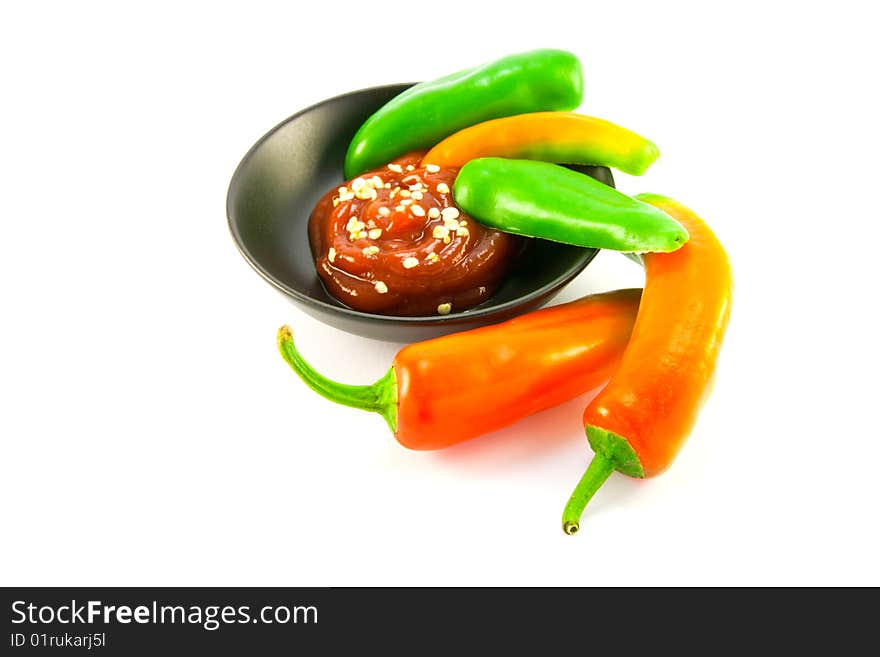 Whole chillis in a black bowl with red chilli dipping sauce and two red chillis outside the bowl with clipping path on a white background. Whole chillis in a black bowl with red chilli dipping sauce and two red chillis outside the bowl with clipping path on a white background