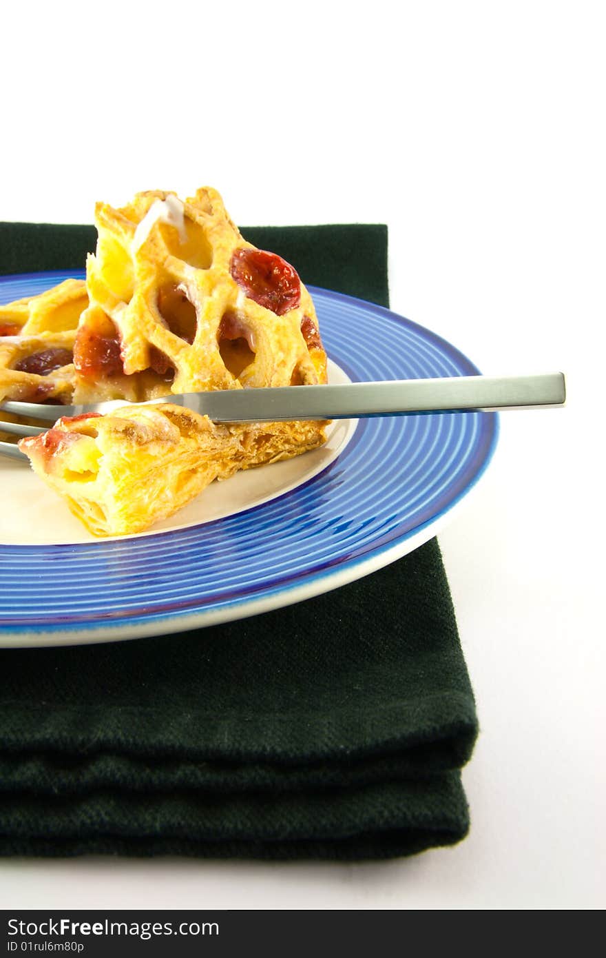 Raspberry and custard danish on a blue and white plate with a fork and black napkin on a white background. Raspberry and custard danish on a blue and white plate with a fork and black napkin on a white background