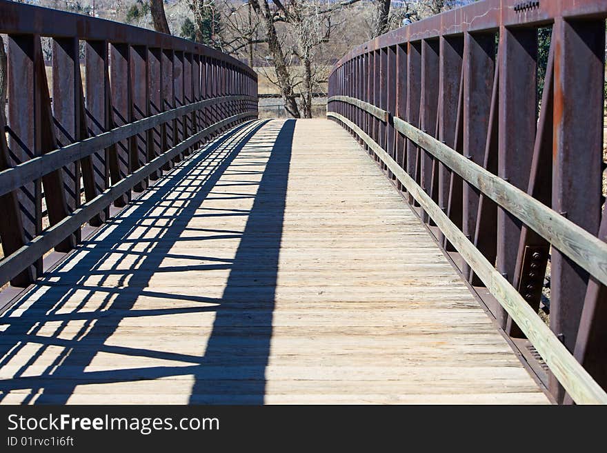 Walkway bridge with wooden footpath and steel trusses, located in a city park.