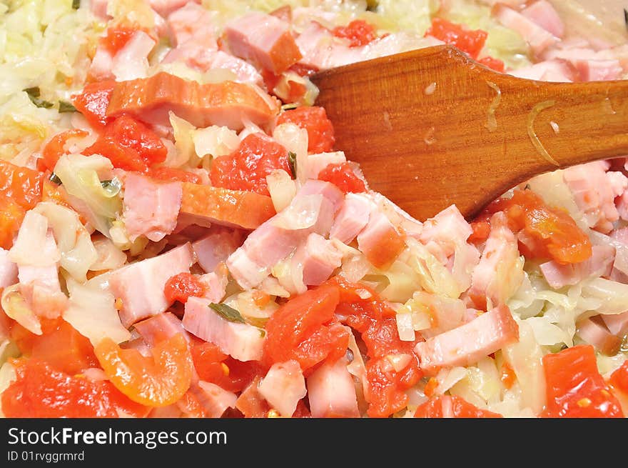 Cooking cabbage with ham an tomato in a pan