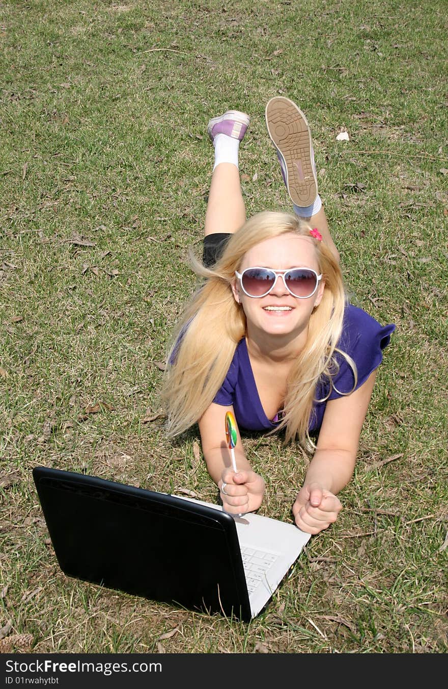 Happy girl with a laptop lying on grass