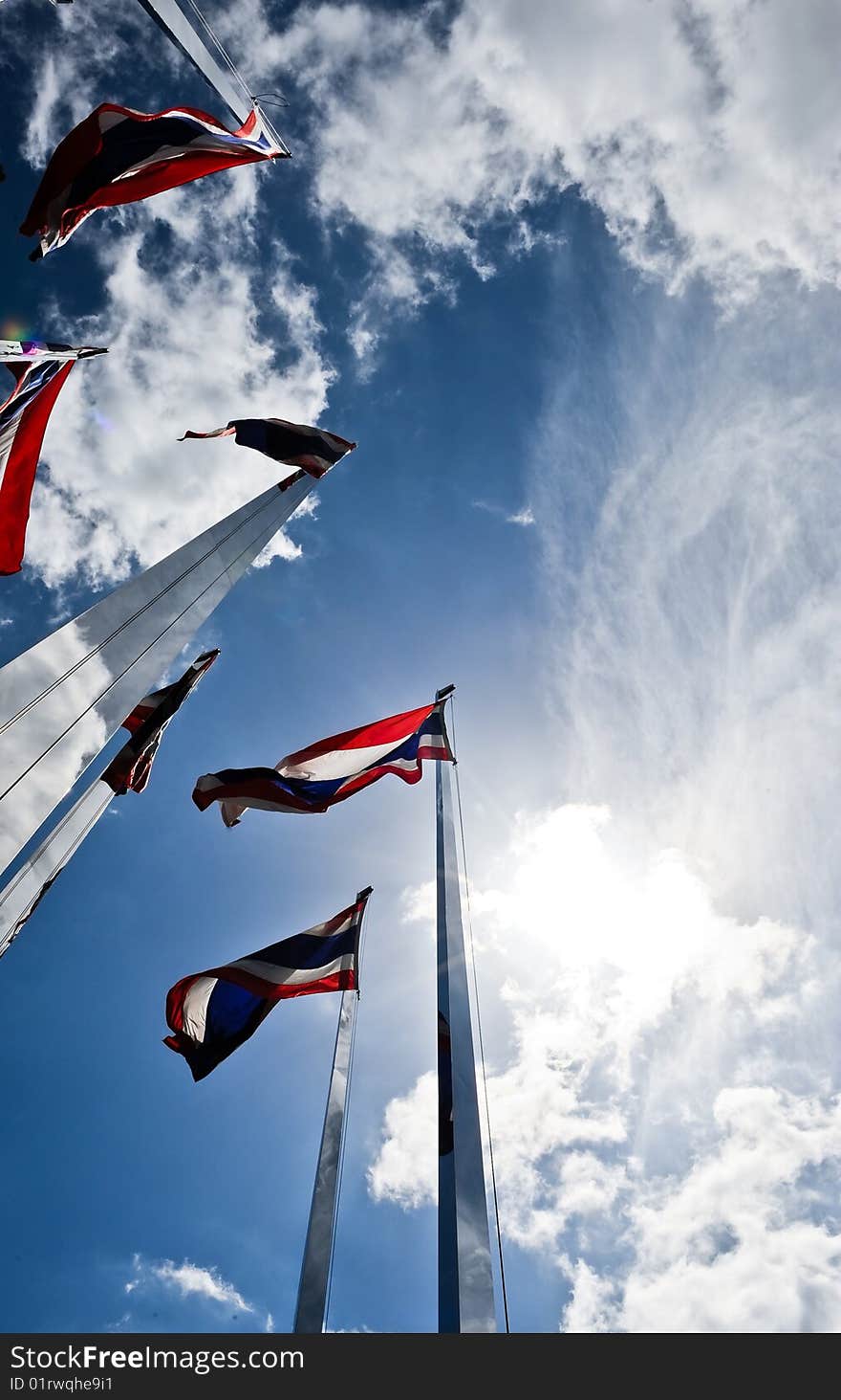 The Thai national flag flutters in the wind under a cloud spattered sky. the sun beams light up the edges of the flags as they flap away. The Thai national flag flutters in the wind under a cloud spattered sky. the sun beams light up the edges of the flags as they flap away.