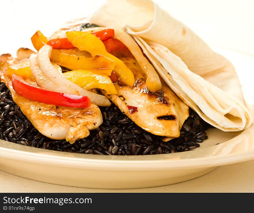 A healthy meal of chicken breast served on black rice with tortillas